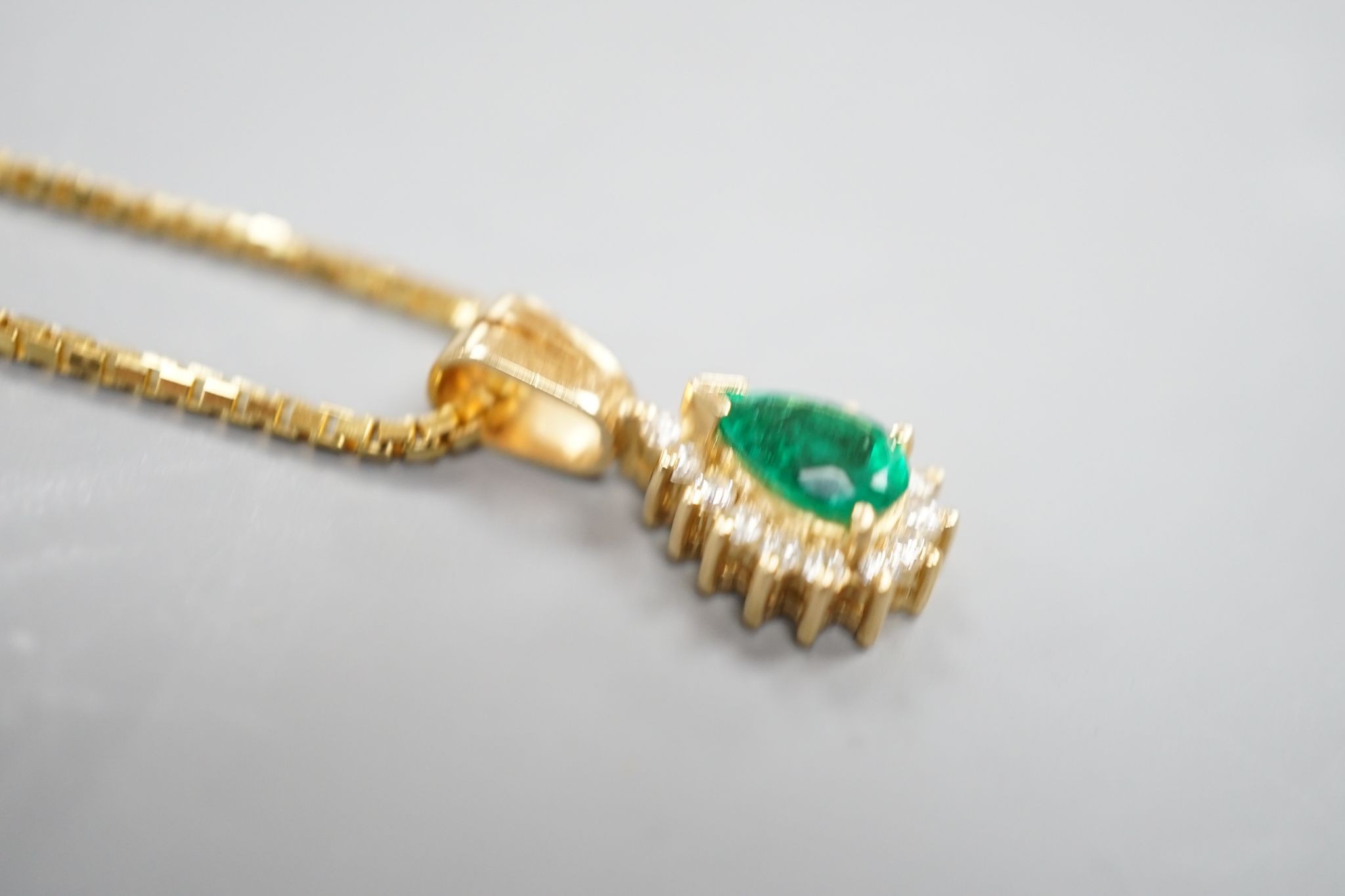 A modern 18k, emerald and diamond cluster set pear shaped pendant, overall 21mm, on an 18k chain, 43cm